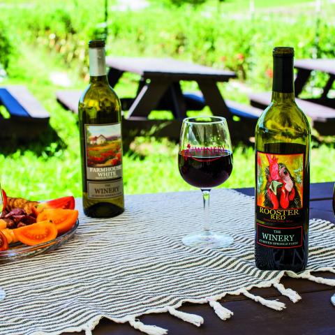 Two bottles of wine, a glass of red and white with a fruit platter on a fringed tablecloth at Winery at Seven Springs Farm